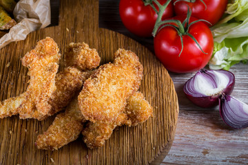 Chicken breast nuggets with vegetables on wooden background. Pile of crispy homemade baked chicken nuggets cooling.