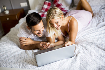Intimate lovers using laptop lying on the bed