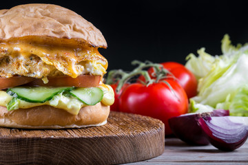 Sandwich with chicken burger, tomatoes, cheese and lettuce on wooden table. Tasty and appetizing hamburger with chicken