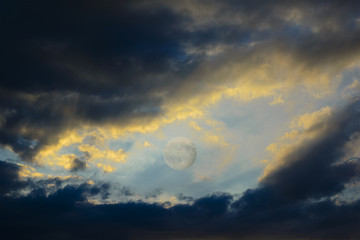 Naklejka na ściany i meble Between the dark clouds backlit by the sunset there is the full moon