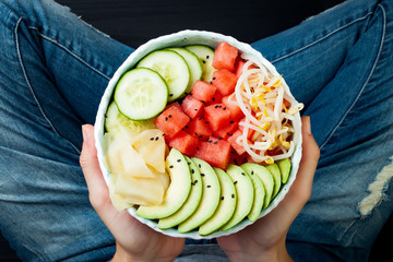 Girl in jeans holding hawaiian watermelon poke bowl with avocado, cucumber, mung bean sprouts and...