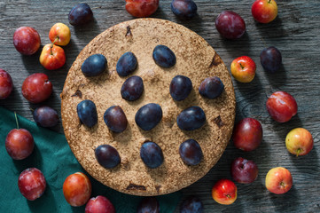 Pie with plum and apples. The cake on the wooden dark table is decorated with fresh plums and apples.