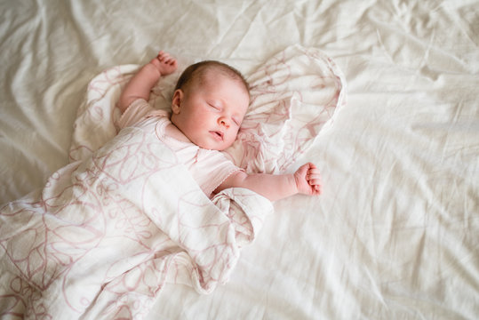 Baby sleeps with arms outstretched and hands closed