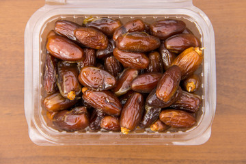 Dried date fruits in plastic container on wooden table. Top view