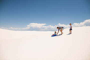 Father pushes daughter on sled down sand hill in White Sands National Monument