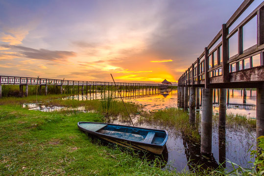 Beautiful golden sunset, row boat and a wooden bridge at pond. Fantastic vivid twilight at Sam Roi Yod National Park, Prachuap Khirikhan, Thailand.