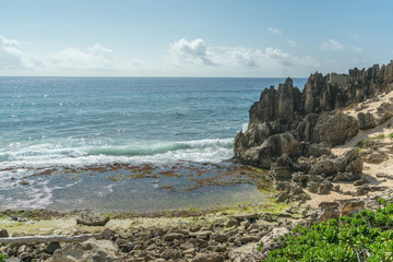 A rocky beach with green shrubs, breaking waves and interesting stone formations above, along the Heritage Trail, on Kauai