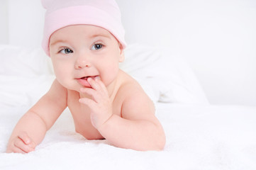 Cute baby lying on a white bedsheet and keeps fingers in his mouth