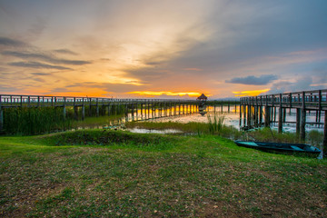 Fototapeta na wymiar Beautiful golden sunset, row boat and a wooden bridge at pond. Fantastic vivid twilight at Sam Roi Yod National Park, Prachuap Khirikhan, Thailand.