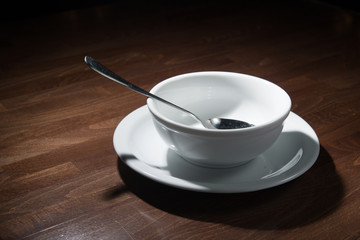 empty white plate with a spoon on a wooden table, symbol