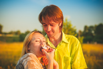 Fototapeta premium Honeymoon couple romantic eatind pie in love at field and trees sunset. Newlywed happy young couple embracing enjoying nature sunset during travel holidays vacation getaway. Caucasian man,woman.