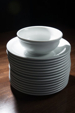 White empty plates stack on a dark wooden table