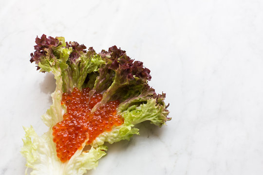 Top view of red caviar on a salad leaf on a light marble background. copy space, Top view. close up