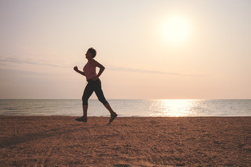 senior woman jogging on sea beach at the sunrise