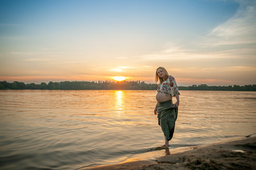 Fototapeta na wymiar A pregnant beautiful woman on the river bank beach smiling with her mehandi ornament belly with love and care. Happy woman on sunset