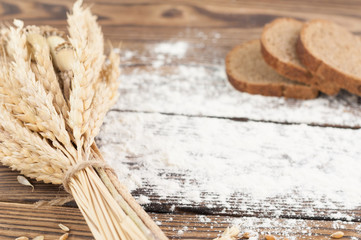 One bundle of wheat and poppy and strewn flour and three slices of bread on old rustic wooden planks