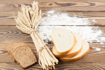 One bundle of wheat and poppy and strewn flour and slices of bread on old rustic wooden planks