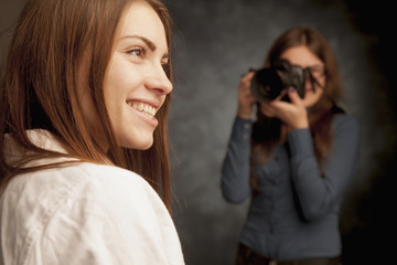 Photo shooting at the studio. Young beautiful female model poses for young woman photographer, photographer taking pictures with a digital camera. Focus on model.