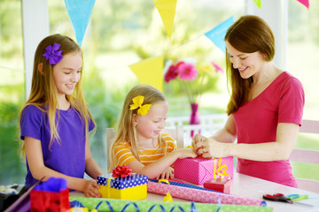 Two cute sisters and their young mother wrapping gifts in colorful wrapping paper