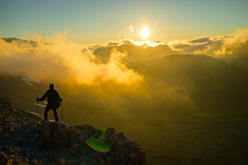 A Person Standing on the Mountain with Clouds During Sunset/Sunrise