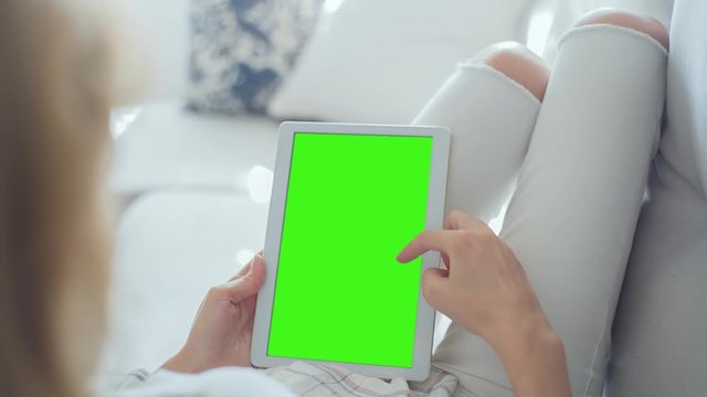 Young Woman in white jeans laying on couch uses Tablet PC with pre-keyed green screen. Few types of gestures - scrolling up and down, tapping, zoom in and out. Perfect for screen compositing