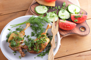 Roasted duck legs with cucumbers, tomatoes and herbs on a white plate