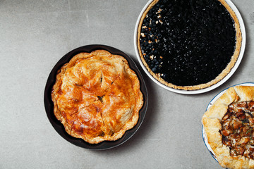Variety of autumn pies: blueberry tart, chantarelle galette and classical apple pie with sweet pastry crust. Harvest time baking concept. Concrete rustic background. Space for text.