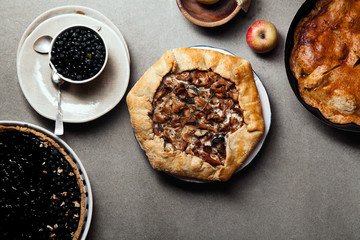 Variety of autumn pies: blueberry tart, chantarelle galette and classical apple pie with sweet pastry crust. Harvest time baking concept. Concrete rustic background. Space for text.