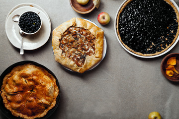 Variety of autumn pies: blueberry tart, chantarelle galette and classical apple pie with sweet pastry crust. Harvest time baking concept. Concrete rustic background. Space for text.