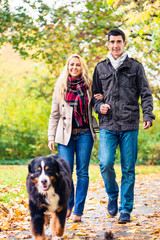 Naklejka na ściany i meble Woman and man with dog having autumn walk on a path covered with foliage