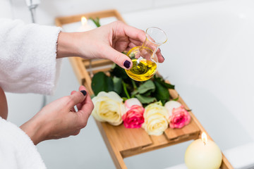 Obraz na płótnie Canvas Woman preparing wellness bath with flowers, candles and fragrance oil in tub