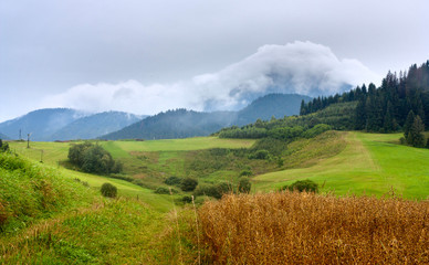 Fototapeta premium Summertime landscape with dirt road and view at covered with white clouds mount Velky Choc (Great Choc), Zilina Region in the Slovakia