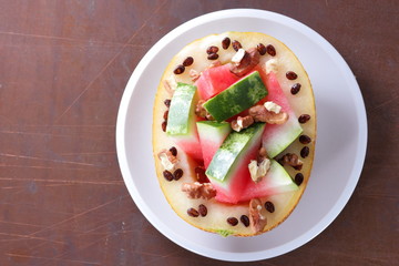 Melon stuffed with watermelon, sprinkled with walnut on a white plate