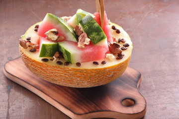 Melon stuffed with watermelon, sprinkled with walnut on a wooden board