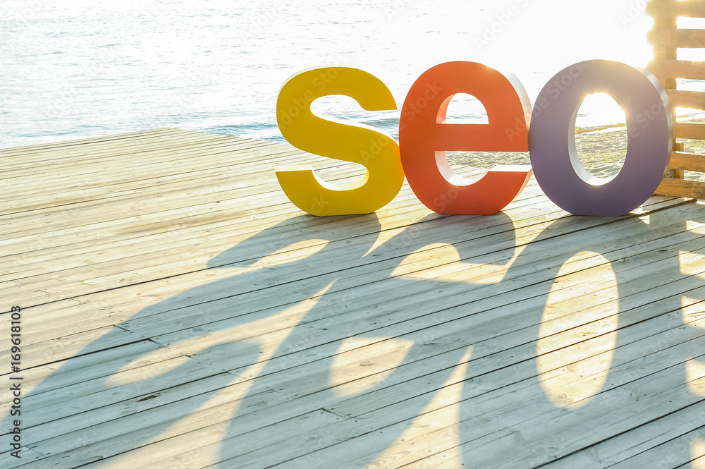 Fototapete the word seo by large colored letters creating a shadow on the wooden terrace on the river bank. sun