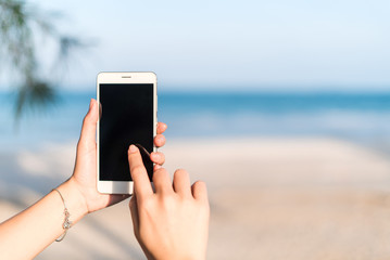 Hand of woman using smartphone mobile, blur the background of the beach.