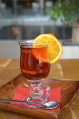 Transparent cup of black tea with slice orange on wooden background.