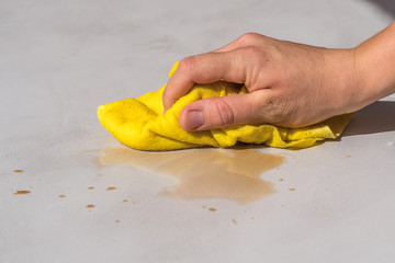 Fototapeta na wymiar woman's hand cleaning tea stain or spilled coffee on a cement floor with a yellow floor cloth dishcloth closeup
