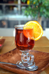 Transparent cup of black tea with slice orange on wooden background.