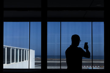 Fototapeta na wymiar silhouette of a young man taking a picture in the airport through a window. Travel concept.