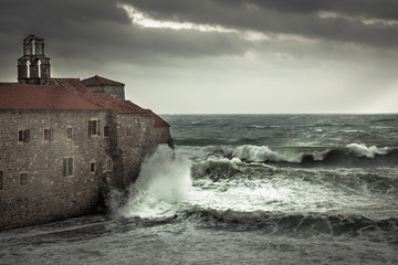 Dramatic landscape with ancient castle on sea shore during storm with big stormy waves and dramatic sky with rain in fall season on sea coast