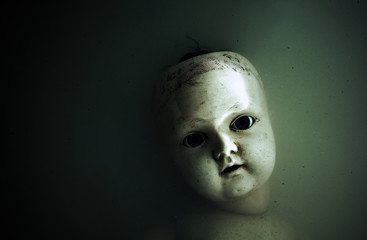 Creepy doll face in dark dirty water