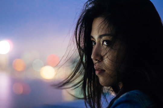 Young woman feeling solemn on a rooftop in Hong Kong at night.