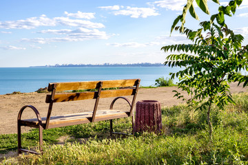 A simple minimalistic layout of a bench on green grass looking out toward the ocean sea beach waters with blue blank empty copyspace sky above the horizon.