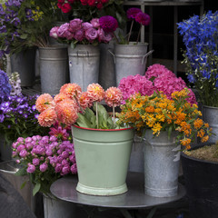 bouquet of dahlias in a galvanized bucket stands on a chair near the entrance to the store.