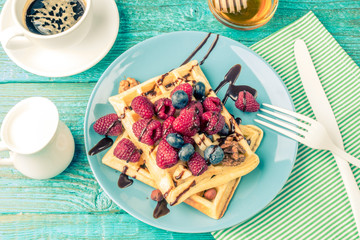Homemade waffles with raspberries and blueberry, cup of coffee, milk and cutlery