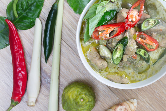 Green Chicken curry in the white bowl and fresh spice seasoning on brown wooden background (Thai food)