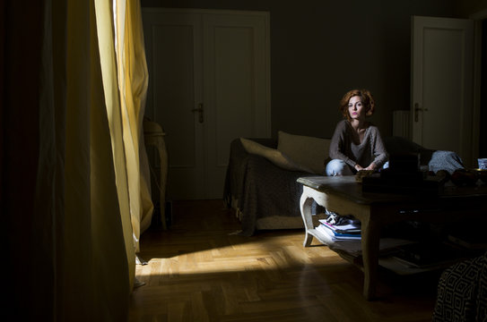 A Young Beautiful Woman Sitting On A Sofa In A Dark Room