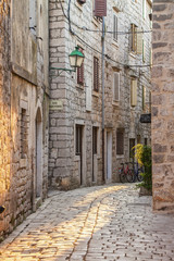 Fototapeta na wymiar Typical Tight Old Street with Green Street Lamps in Ancient Town Stari Grad in Croatian Island Hvar