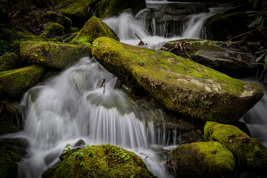 Close Up Of Rushing Water Around Mossy Boulders